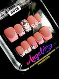 Set of decorative nail art with pink and white designs in a clear display case, featuring the brand 'Angel'.