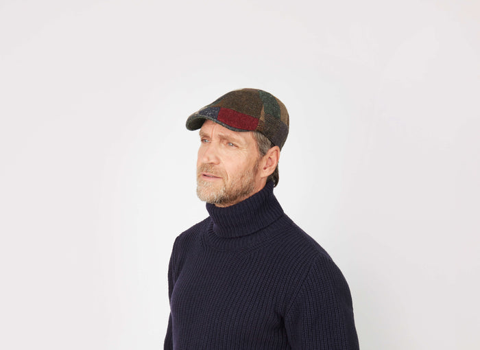 A bearded man in a dark turtleneck and the Hanna Hats Erin Cap Patchwork Tweed gazes slightly to the side against a plain white background.