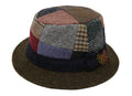 The Walking Hat Patchwork Tweed by Hanna Hats is a wool hat inspired by Donegal heritage, featuring colorful tweed fabrics, a dark brim, and a brown decorative feather.